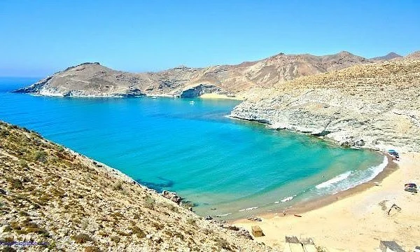 Agua turquesa en una bahía resguardada con una playa de arena y colinas escarpadas y rocosas