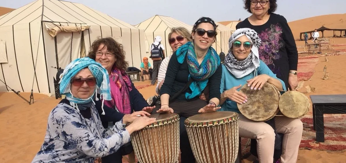 Guests playing traditional drums at a Merzouga desert camp during a 3-day tour from Fes