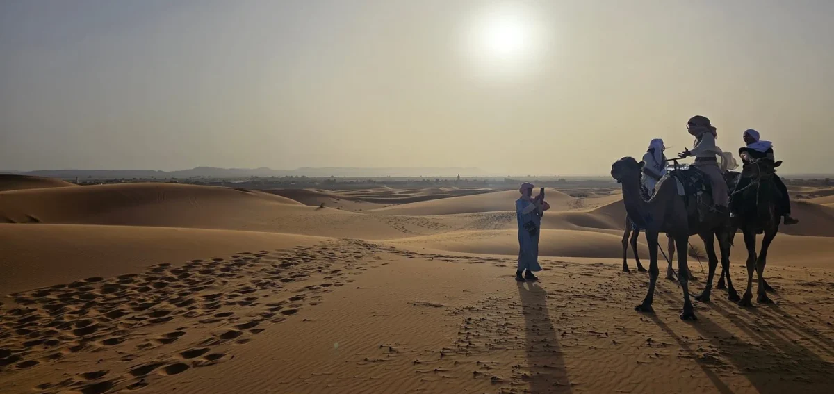 Travelers riding camels at sunset across the Erg Chebbi dunes during the 4-day Agadir to Merzouga desert tour