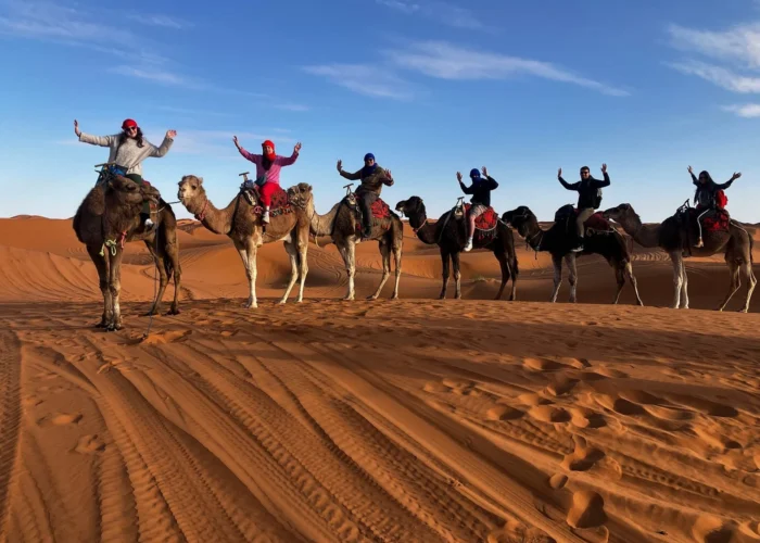 Viajeros montando camellos por las dunas de Merzouga durante un tour de 9 días de Tánger a Marrakech