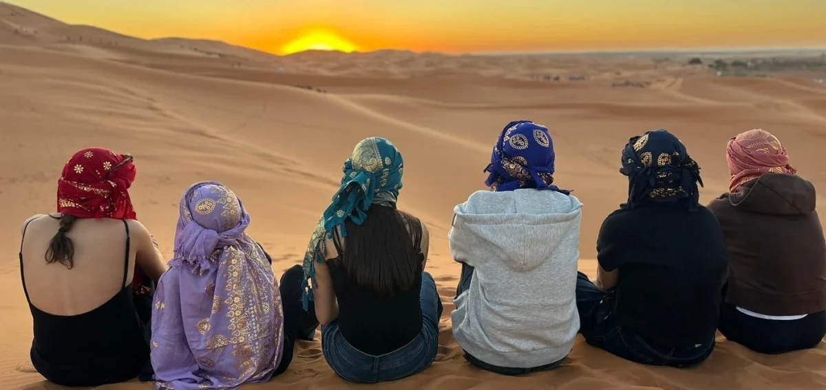 Travelers watching sunset in the Merzouga Desert during an 8 days Morocco tour from Casablanca to Marrakech